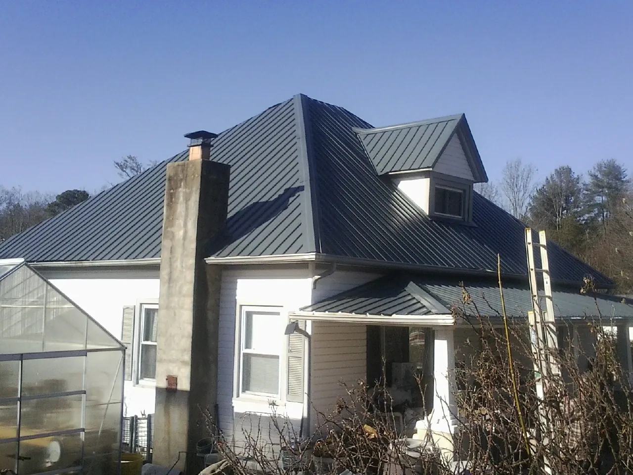 Dark blue standing seam metal roof on a white farmhouse with dormer — Slate & Tile Roof Repair by Roofing Brothers in Higden
