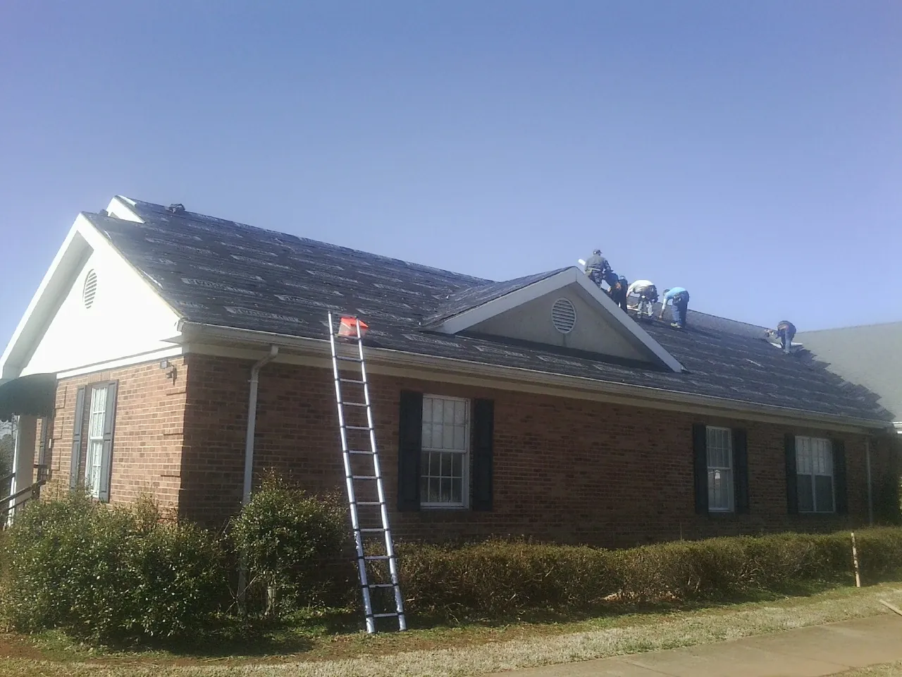 Crew tearing shingles off a brick ranch roof with a ladder set — Metal Roof Repair work by our crew in Higden