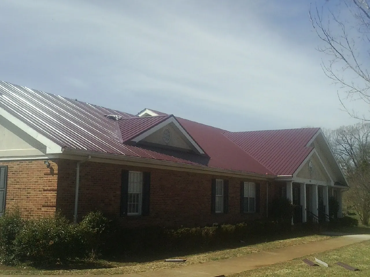 Red metal roof with gabled entries on a long brick building, from a Hail Damage Roof Repair job in Higden