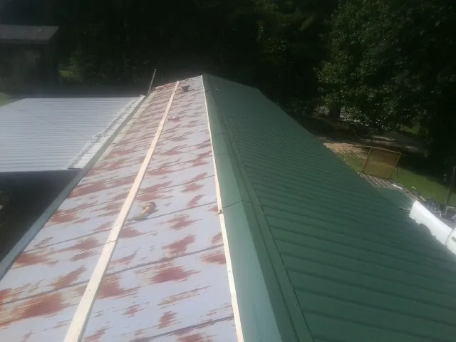 Old rusted panels beside newly installed green metal roofing — Wind Damage Roof Repair by Roofing Brothers in Higden