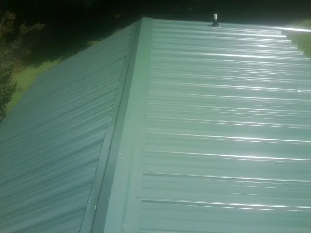 New green metal panels meeting at the ridge of a roof — Flat Roof Repair work by our crew in Higden