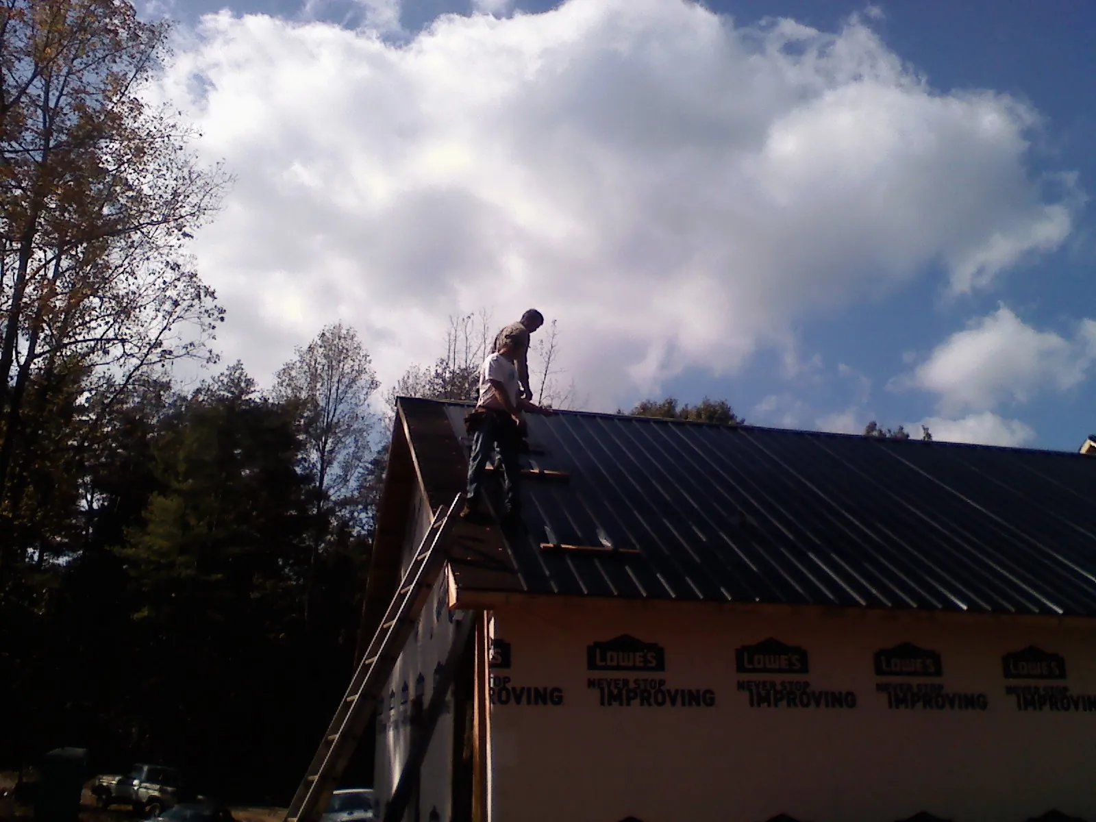 Roofer fastening dark metal panels high against a cloudy sky, from a Roof Inspection job in Higden