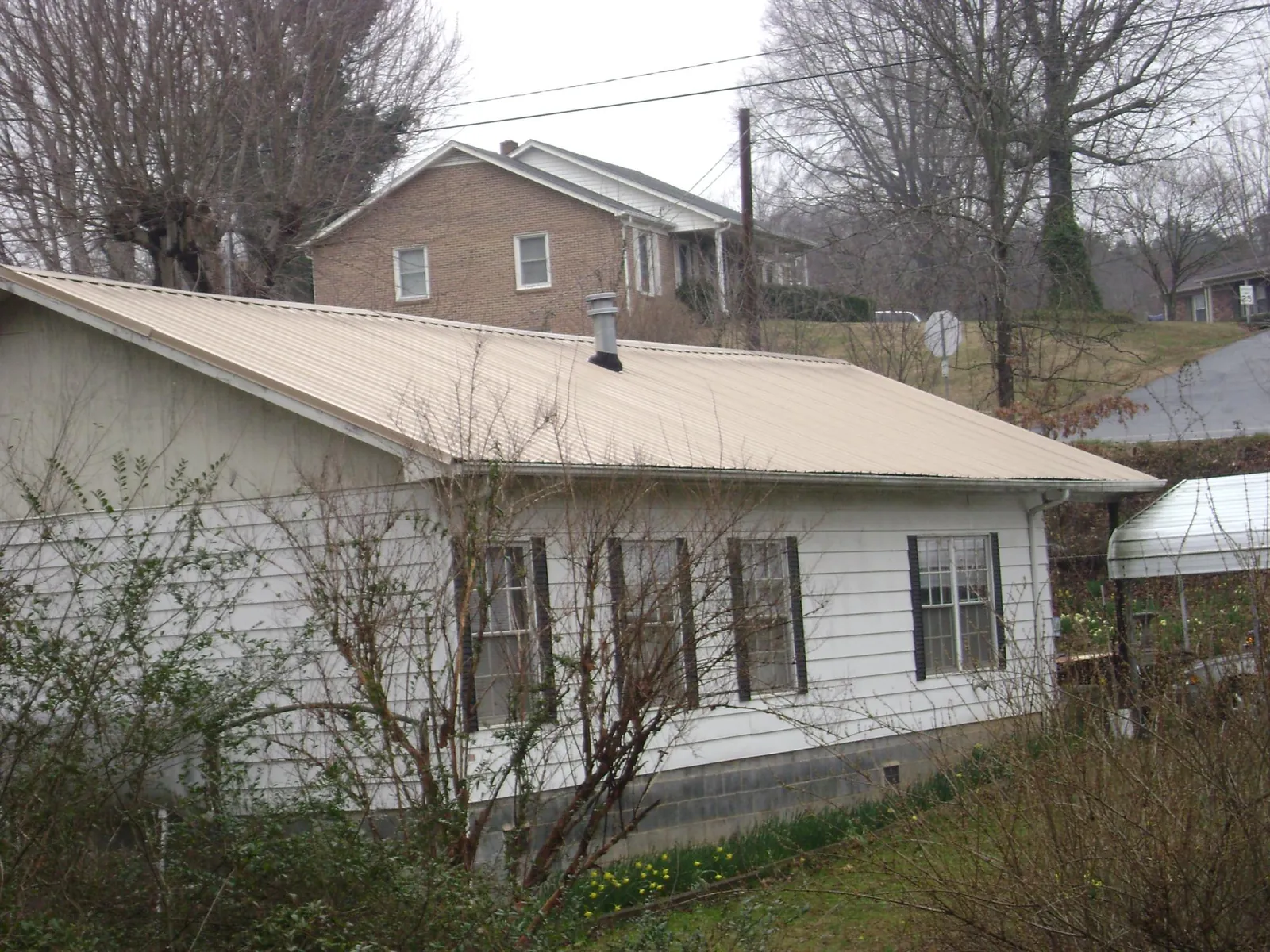 Tan metal roof on a white sided house set into a hillside — Commercial Roofing by Roofing Brothers in Higden
