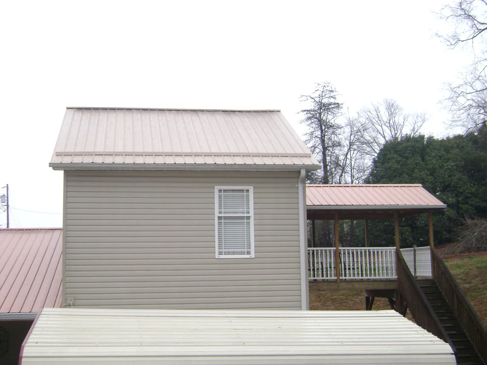 Tan metal roofs on a two story addition and attached porch, from a Roof Replacement job in Higden